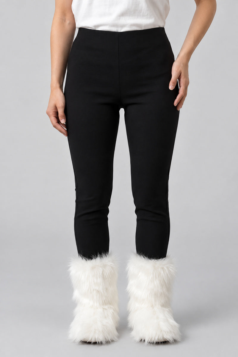 Bottes en moumoute blanches portées avec un pantalon noir, vue de face sur fond gris clair.