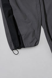 Jogging Y2K édition 'Shadow Sport', détail de l'ourlet réglable, sur fond studio gris clair.