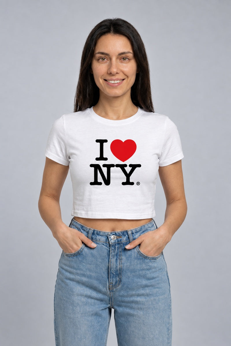 Baby tee blanc I Love NY avec cœur rouge, porté de face, mains dans les poches.