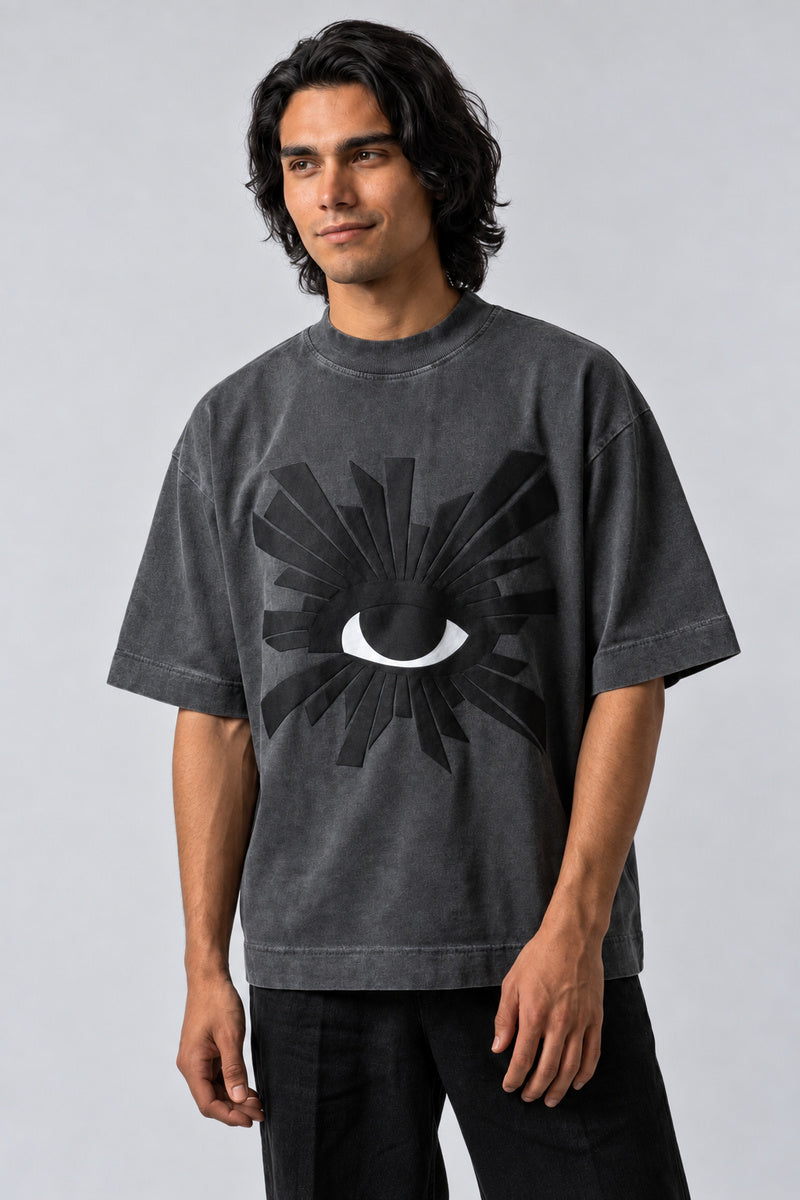 T-shirt gris oversize avec grand œil blanc entouré de rayons noirs en relief, vue de face.