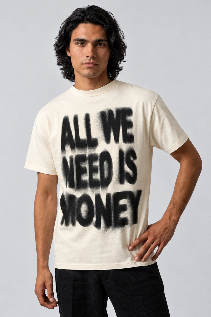 T-shirt écru avec inscription noire « All We Need Is Money », porté de face sur fond gris perle.