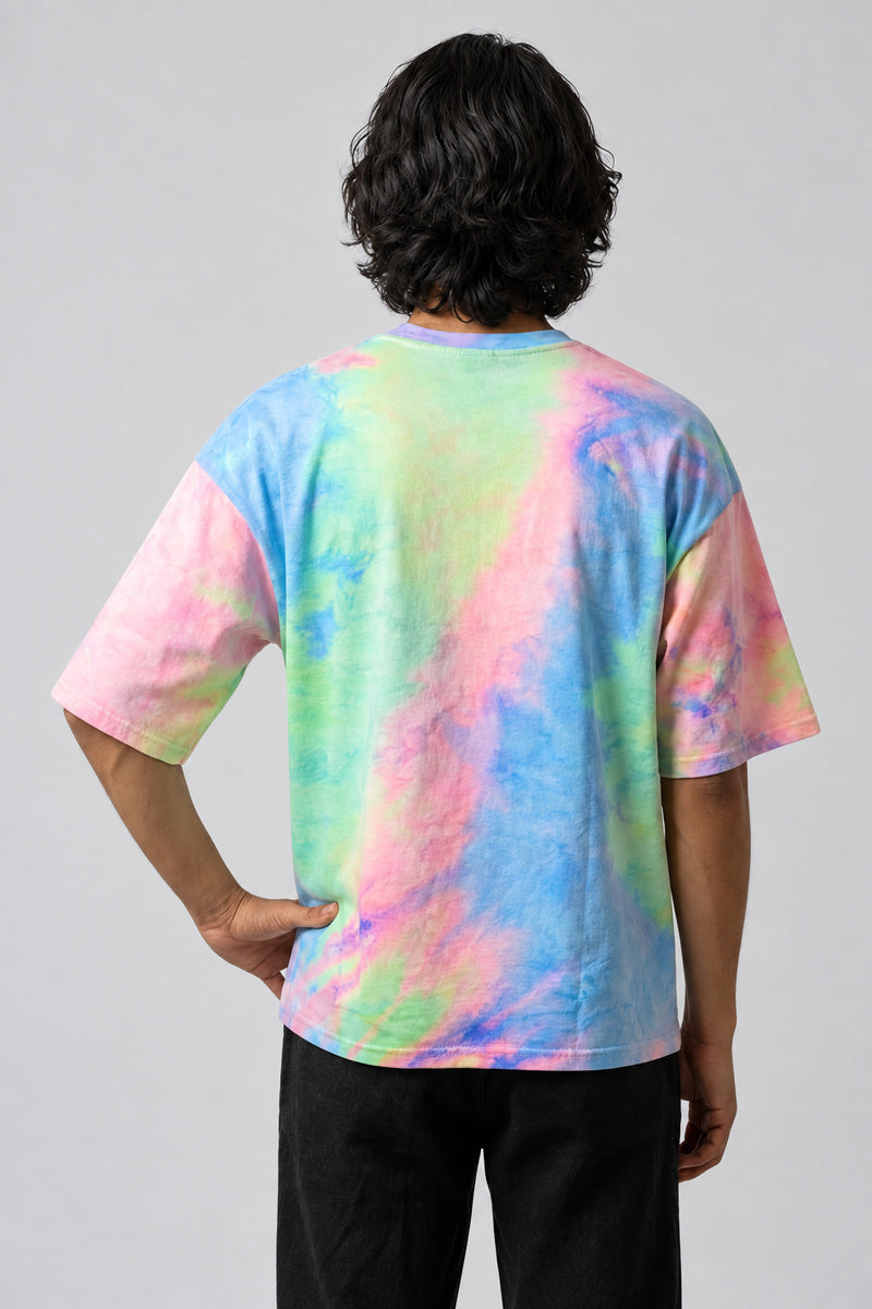 T-shirt tie-dye pastel multicolore vu de dos, avec une main sur la hanche.